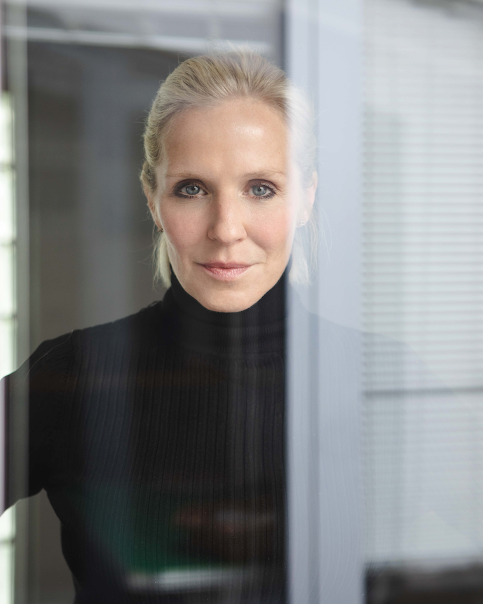 Loni Baur schaut auf einem Portraitfoto durch eine Scheibe.