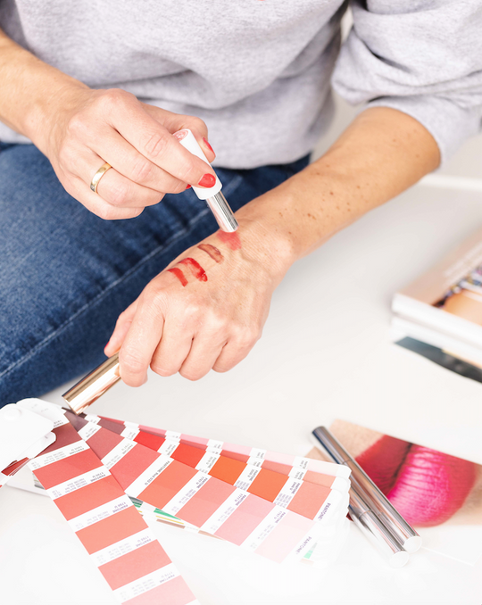 Loni Baur testet verschiedene Lippenstiftfarben auf ihrem Handrücken und vergleicht diese mit Farbkarten.