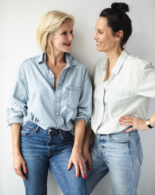 Loni Baur und Nike Lohmann sind die Gründerinnen der Marke LONI BAUR. Sie stehen im Büro und lächeln sich an.